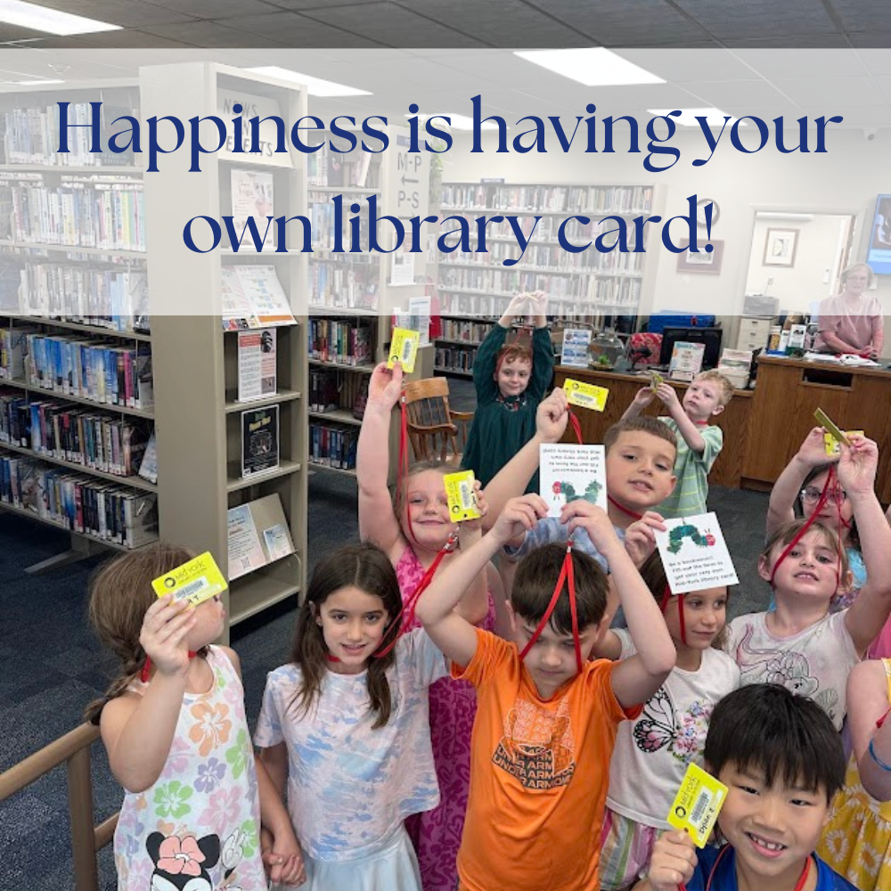 A photo of first grade children holding up their first library cards. Across the top of the photo it says Happiness is having your own library card!