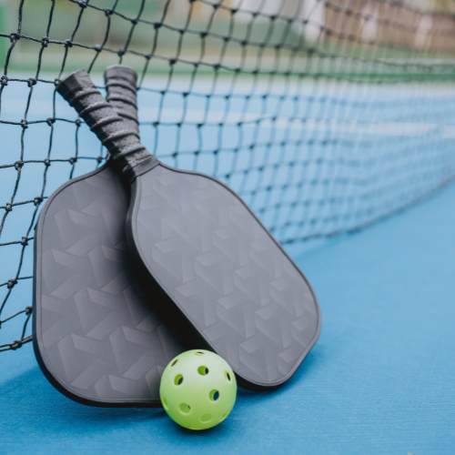 Two rackets leaning against. a net with a pickleball between them.