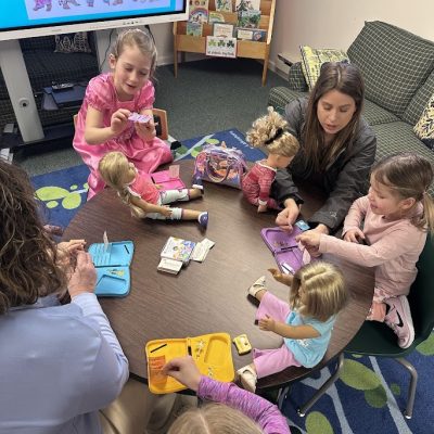 A picture from our American Girl Pajama Party. It shows a group of girls gathered around a table with their dolls. They are doing a craft.
